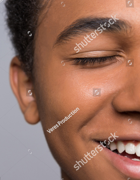 This is a very close up photo of a young person's face.  You see only the left side of the face and the gender of the person is unknown.  Their eyes are closed and they have a smile on their face.