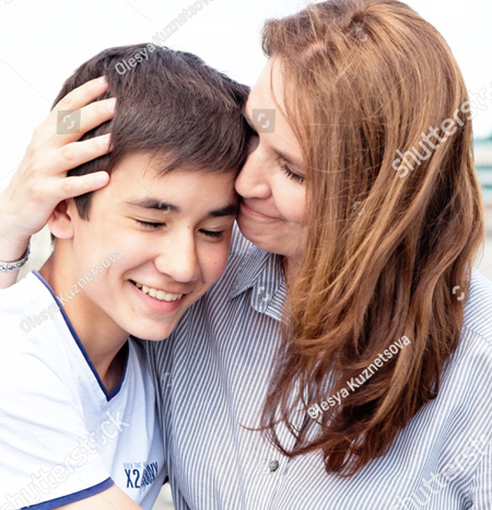 A photo of what appears to be mother and son.  The mother is on the right and she has her right hand around the back of the boy's head and she is holding his head.  She is wearing a blue and white striped shirt and has a smile on her face.  The boy is leaning into his mother and has a smile on his face. His eyes are also closed. He is wearing a white t shirt.